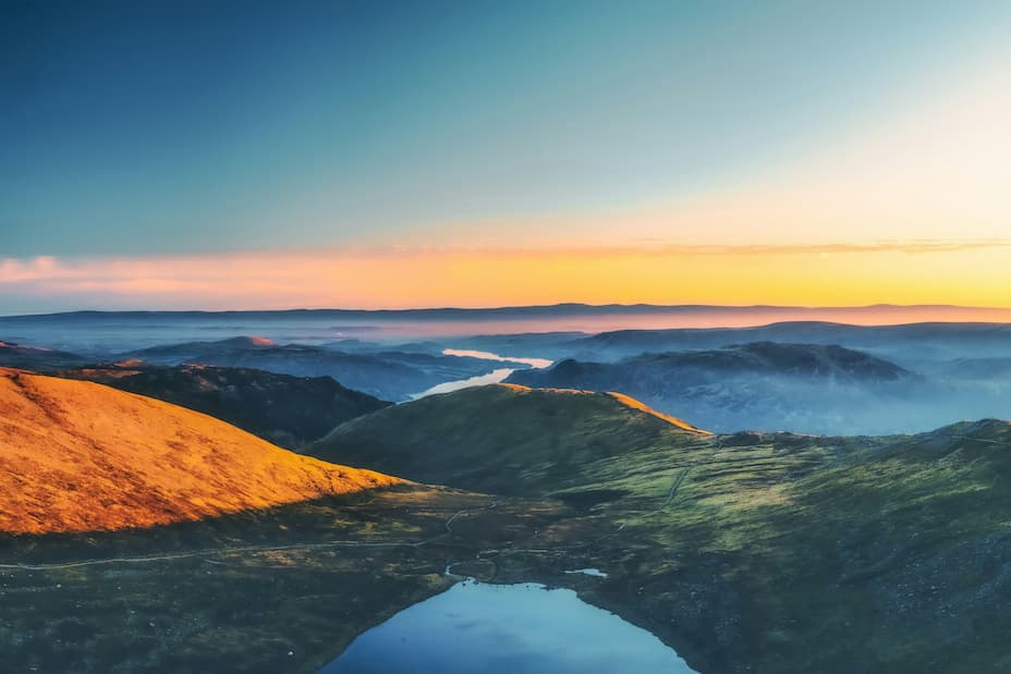 A view of the fells with mist hanging in the valleys and the sunrise casting a warm light